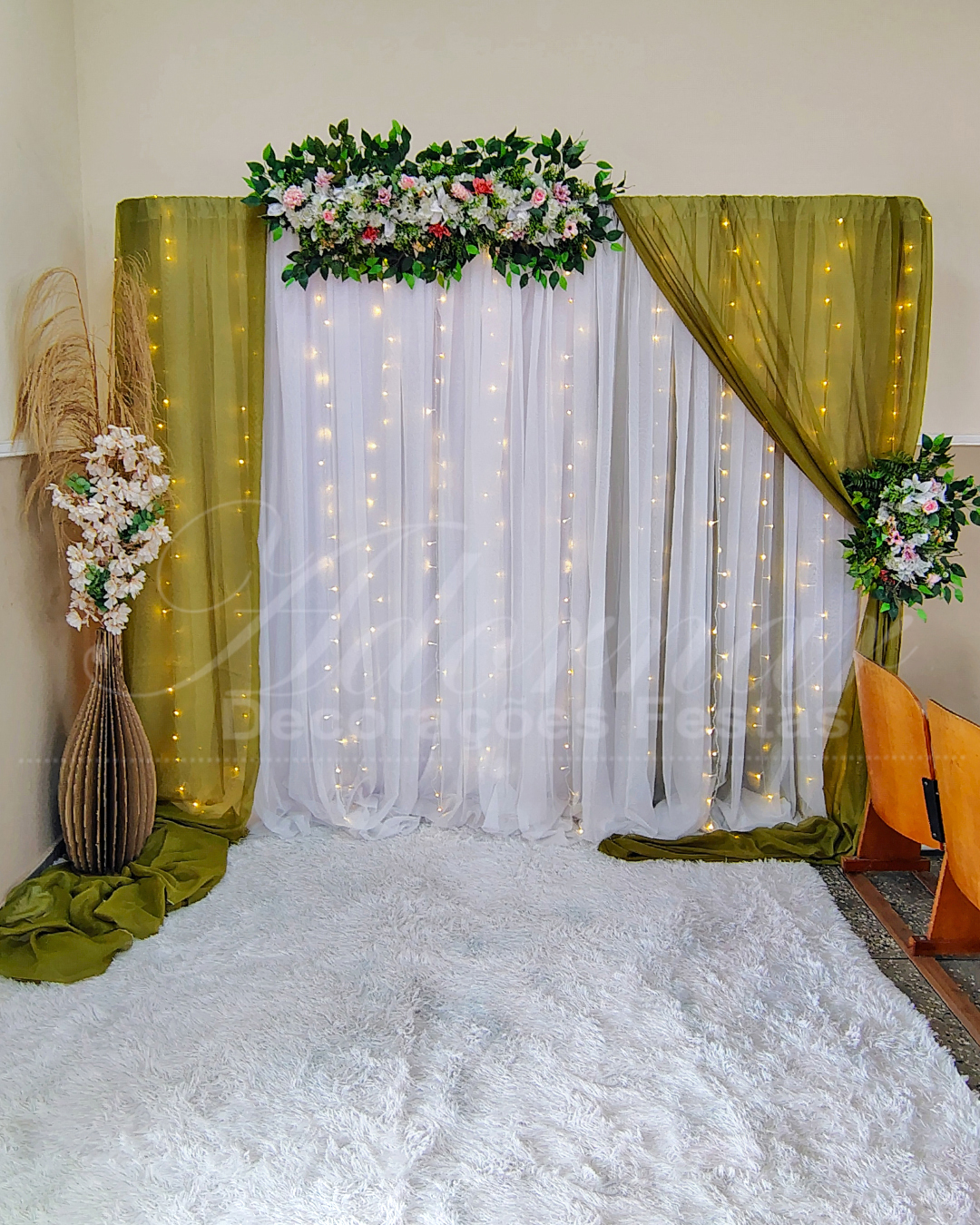 Backdrop elegante para casamento com painel verde oliva iluminado, vaso decorativo de chão e arranjo de capim dos pampas